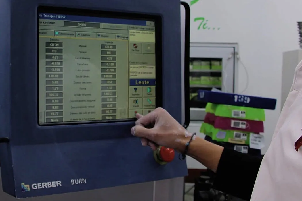 Mano tocando la pantalla de control de una máquina Gerber con los parámetros de la lente en pantalla