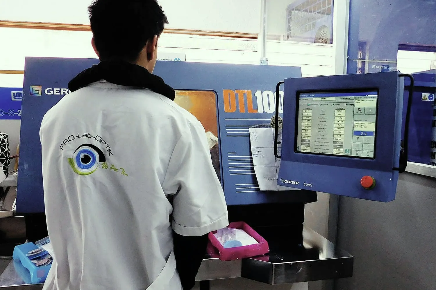 Técnico con bata del laboratorio, de espaldas, frente a una máquina de tallado Gerber DTL100